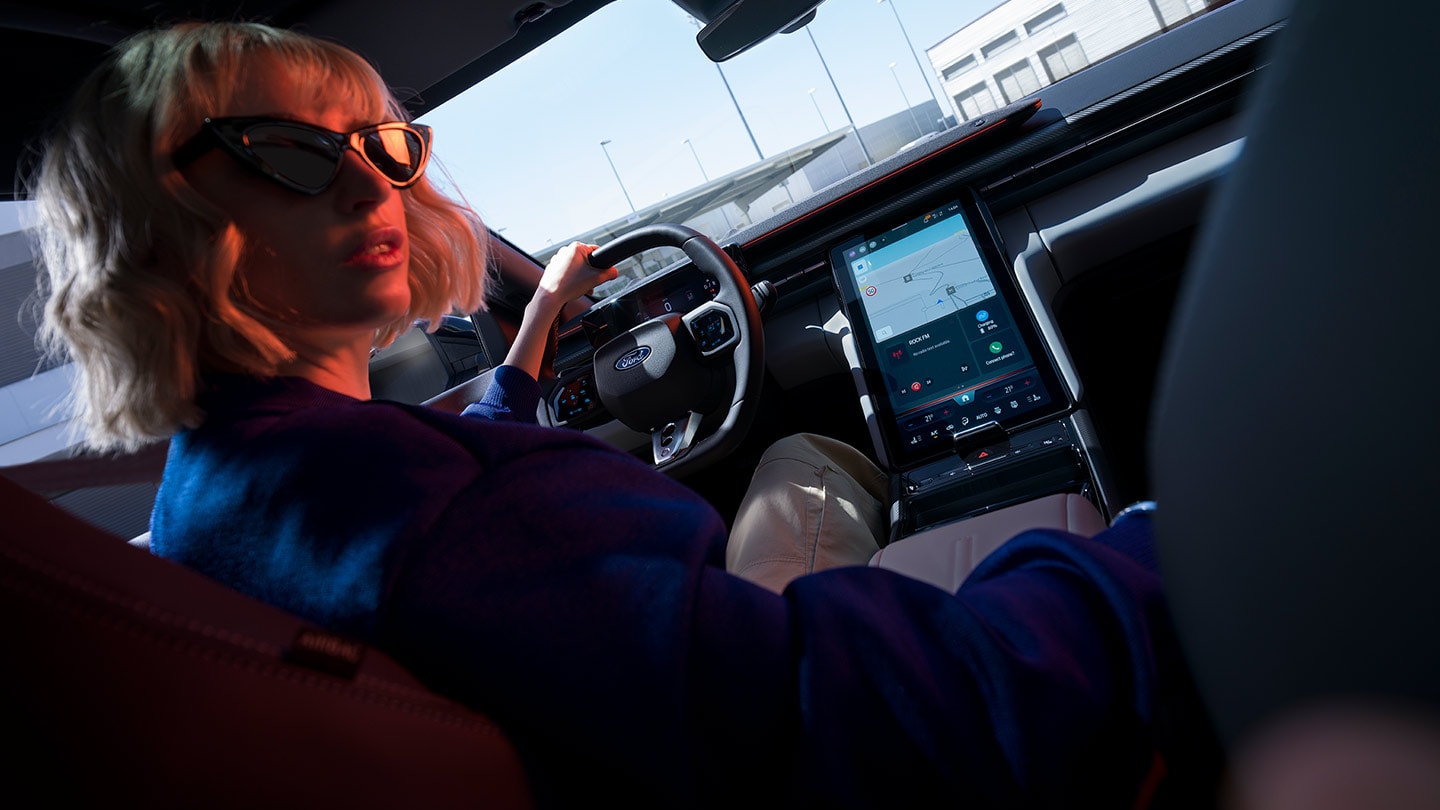 Vrouw aan het stuur van de nieuwe Ford Capri® met zicht op het stuurwiel, het dashboard en het grote SYNC® Move-touchscreen.