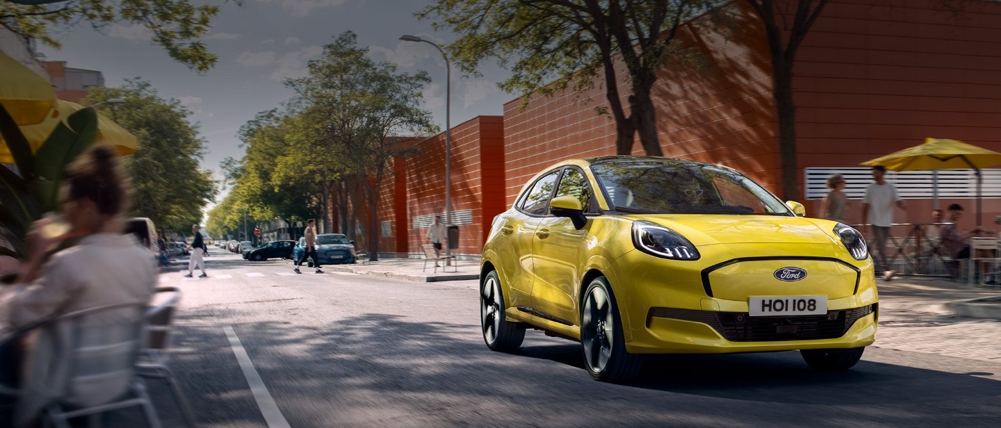 Vooraanzicht van een gele elektrische Ford Puma Gen-E® die langs een stadsweg rijdt